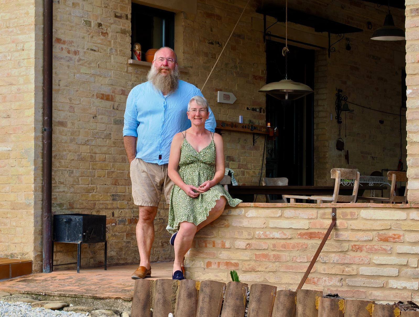 Een portret van de eigenaren van B7B La Villa angelica zittend op een murrtje van de portico (overkapping).